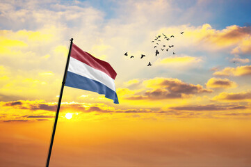 Waving flag of Netherlands against the background of a sunset or sunrise. Netherlands flag for Independence Day. The symbol of the state on wavy fabric.