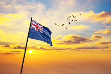 Waving flag of New Zealand against the background of a sunset or sunrise. New Zealand flag for Independence Day. The symbol of the state on wavy fabric. - obrazy, fototapety, plakaty