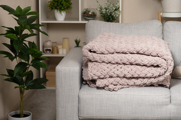 Knitted large plaid blanket in dusty rose light grayish-red color on the sofa.