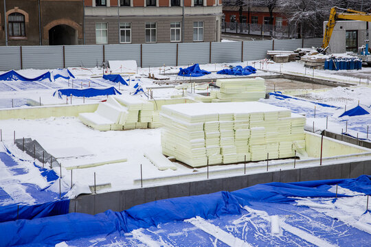 construction site in winter with stacks of insulation boards and blue protective tarps against snow