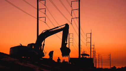 Silhouette of excavator and bulldozer tractor working overtime to leveling the ground near country roadside with row of electric poles against colorful evening sky after sundown, perspective side view