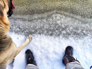 Feet of Hunter or fisherman in big warm boots And paws of dog on snow. Top view. Fisherman on ice...