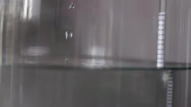 alcohol distilling process closeup - liquid distilled transparent liquid flowing in large glass jar with floating alcoholometer in it.