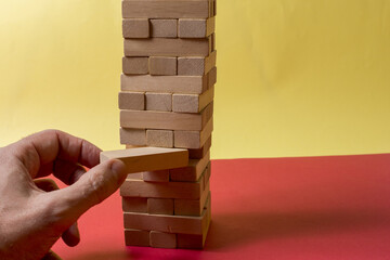 Closeup image of a hand holding and playing Jenga or Tumble tower wooden block game