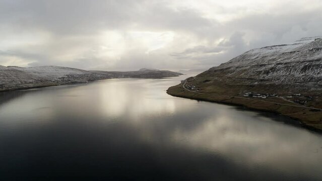 Faroe Islands, 4K Aerial of town perched on the edge of the water with beautiful cloud and sunshine reflections