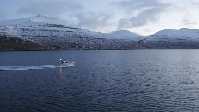 Faroe Islands, 4K Aerial tracking three quaeter shot of fishing boat with snow covered mountains in the background