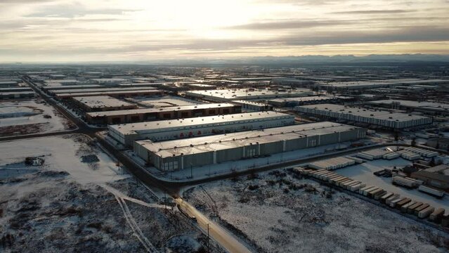 Giant warehouses covered with snow in the middle of winter with the Rocky Mountains in the background.