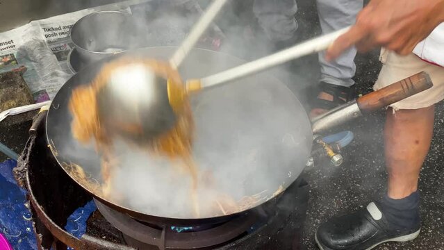 Street food vendor cooks a stir fry noodle dish using a wok pan at Chulia street, George Town, Penang, Malaysia.