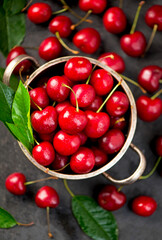 Ripe sweet cherry berry with leaves in a pan on a black wooden board
