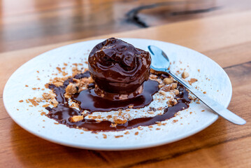Delicious ice cream scoop on plate close-up with melted chocolate dressing and hazelnuts on a rustic wooden table