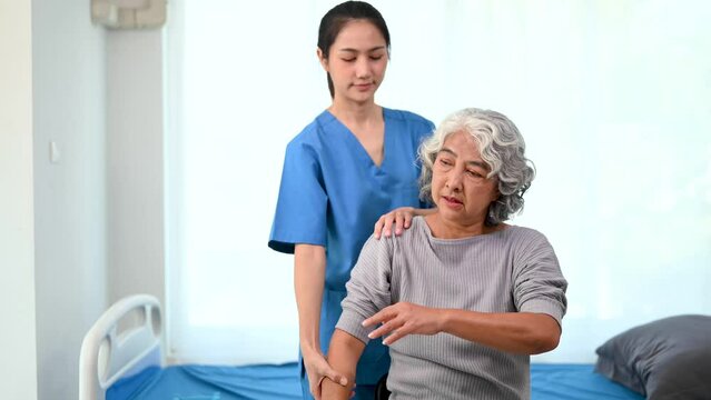 Asian physiotherapist helping elderly woman patient stretching arm in hand during training hand with patient Back problems in bed