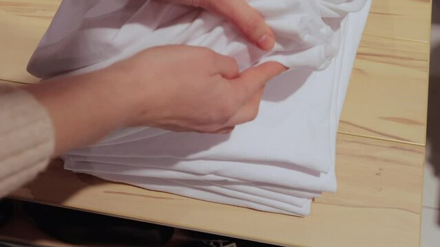 Unrecognizable woman in fashion boutique browsing stack of white T-shirts looking for correct size buying new clothing for summers to her basic wardrobe