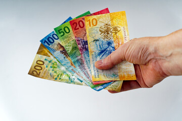 Close-up of caucasian woman hand holding five Swiss banknotes in her hand against white background....
