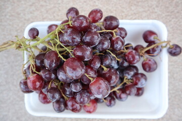 Freshly picked red grapes placed on a white plate.