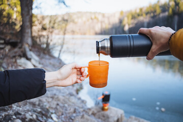 Drinking hot tea in nature, guy pouring coffee into a glass for a girl against the background of a...