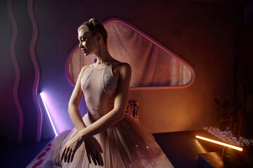 Medium full shot of young caucasian ballerina posing in creative art space with dim neon lights