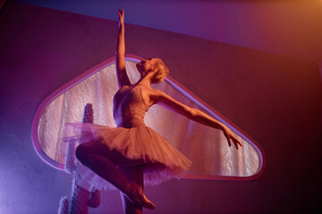 Ballerina standing on one leg with outstretched arms showing ballet move in studio under neon lights