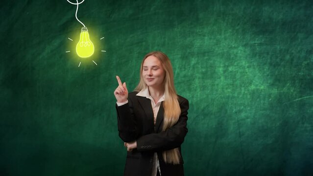 Portrait of woman isolated on green background light bulbs image on top. Girl standing pointing finger at lighted yellow bulb, smiling expression, found idea.