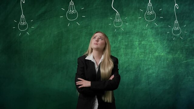 Portrait of woman isolated on green background light bulbs image on top. Girl standing thinking looking up with praying gesture, no ideas lamps without light.
