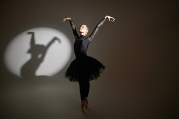 Ballerina demonstrating dance figure during studio photoshoot, her shadow cast on background on left