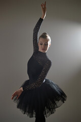 Ballerina in black lace leotard and tutu standing in static ballet pose during photoshoot in studio