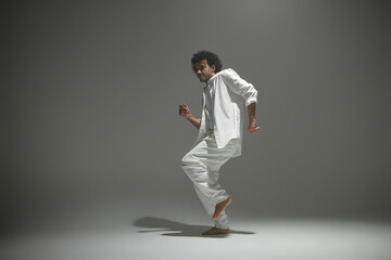 Fototapeta na wymiar Young man in white outfit lightly dancing on photoshoot set