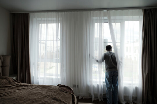 Man looking through window in bedroom at home