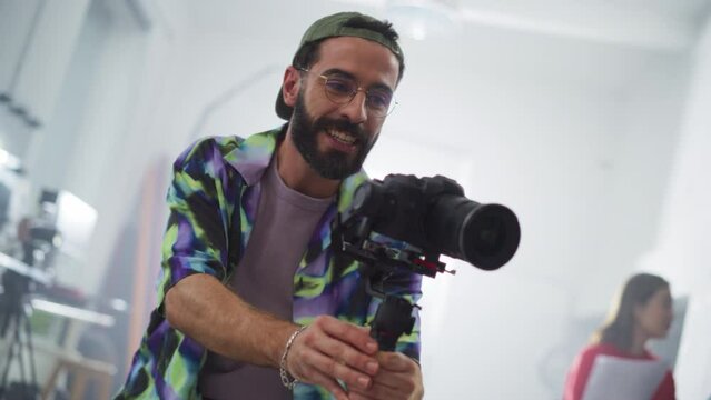 Slow Motion Portrait of a Male Videographer Using a Stabilizer on a Set and Giving Directions to a Model While Filming a Commercial. Artist Using Digital Camera For Making a Video as Creative Project