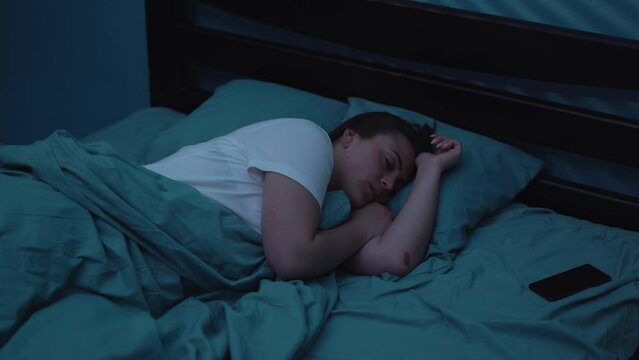 Woman sleeping on bed at night wakes up with alarm from mobile phone ringing in her bedroom