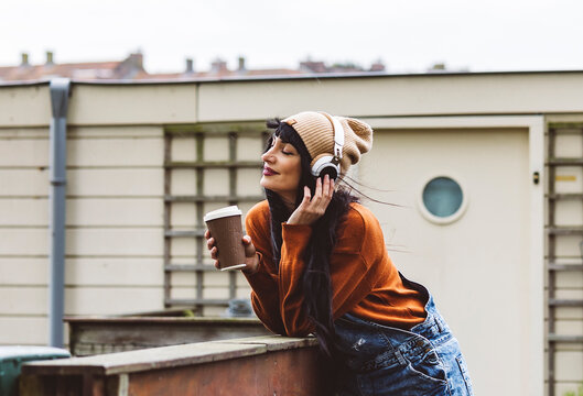 Smiling Woman Holding Coffee Cup And Enjoying Music Through Wireless Headphones