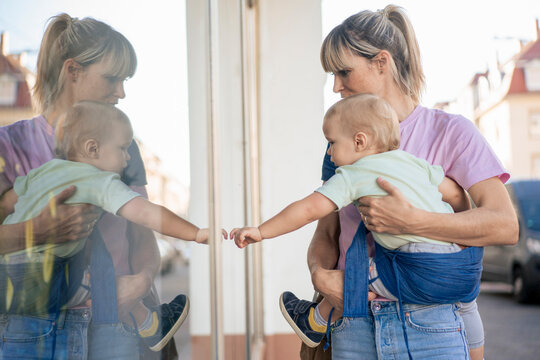 Mother carrying son touching store window at street