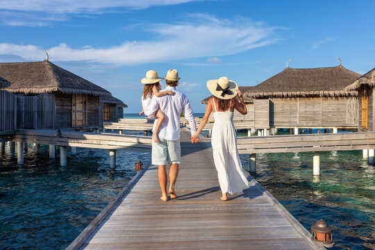 A beautiful family walks over a wooden pier between water lodges in the Maldives islands during their vacations