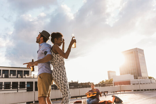 Man with woman holding beer and dancing on rooftop