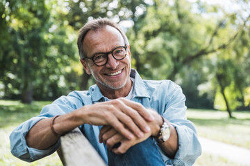 Smiling senior man with eyeglasses sitting on bench in park