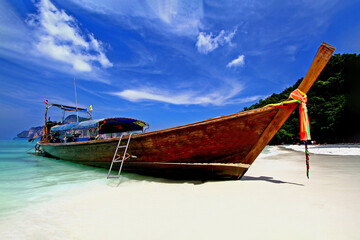 Fototapeta na wymiar Big long tail boat parking on the white sand beach with blue sky and white clouds at Phi Phi island Krabi, Thailand.