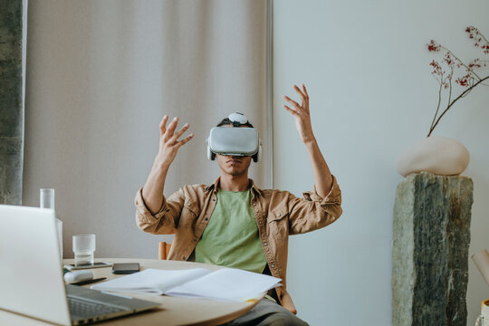 Young man wearing VR headset sitting with arms raised at table
