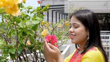 A young Indian woman smells Bougainvillaea flowers - beautiful smile  stress-relief  mental health  scent. Asian girl relaxing and connecting with nature - spiritual healing  mood booster  emotiona...