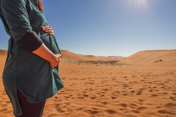 Travelling pregnant - close up of a woman holding her belly in front of the sand dunes of sossusvlei, namibia