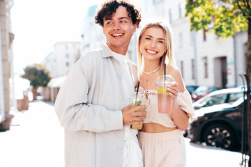 Young smiling beautiful woman and her handsome boyfriend in casual summer clothes. Happy cheerful family. Female having fun. Couple posing in street. Holding and drinking cocktail drink in plastic cup