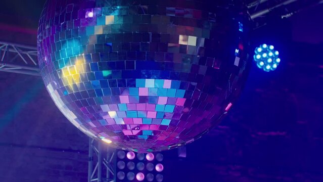 A large disco ball is spinning against the background of the stage with lighting devices illuminating it with colored yellow rays of light. A beautiful glass ball at a renault dance party at the club