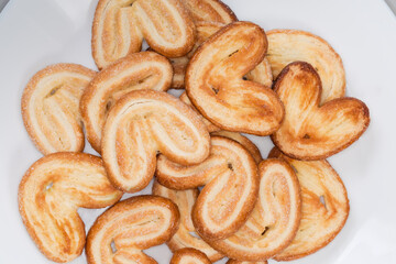 Heap of puff pastry butterfly cookies on dish, top view