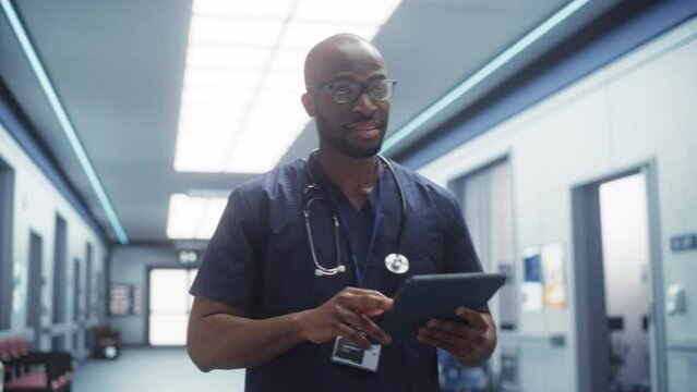 Following Shot of a Male Doctor with Positive Attitude, Calmly Walking Through Hospital Hallway, Using Digital Tablet, Greeting Nurses and His Colleagues. Bright Modern New Clinic