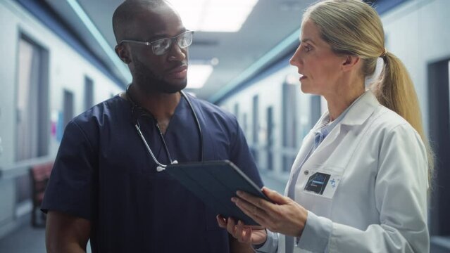 Health Care Medical Hospital. Professional Black Male Nurse and Female Doctor Walking Through Hallway, Talking, Use Digital Tablet Computer, Discuss' Patient Treatment, Drugs or Therapy