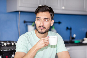 Thoughtful man sitting at the table in the kitchen and drinking hot coffee