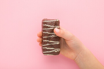 Baby girl hand holding and showing bar with dark brown chocolate glaze and white stripes on light...