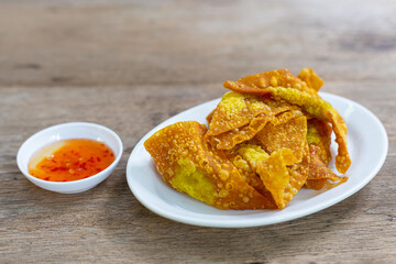 Delicious Thai style crispy homemade fried pork dumplings in white ceramic plate with dipping sauce in ceramic cup delicious Thai appetizers on wooden table.