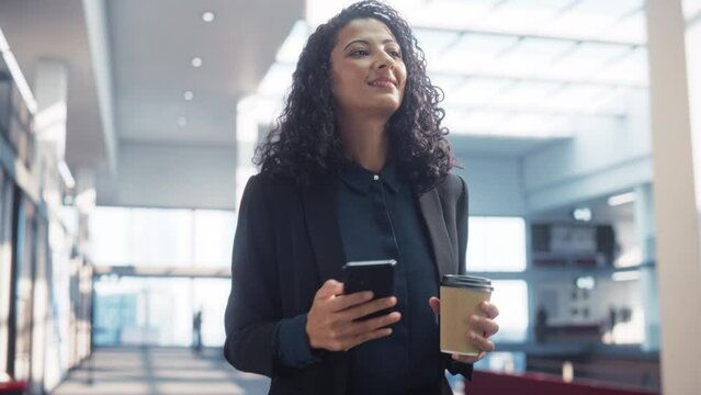 Portrait of a Happy Multiethnic Woman Texting on her Smartphone and Walking in Corporate Office. Confident Female Marketing Manager Checking Social Media Trends and Staying Updated