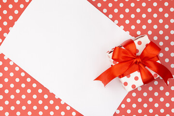Obraz premium Red polka dots gift or present box with bow with paper on pattern background. Birthday, Valentine's, Mothers's and Women's day, holiday. Copy space