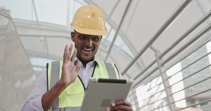 Male American engineer standing using tablet to inspect building construction technology Off-site online meeting. blue collar professional. online communication