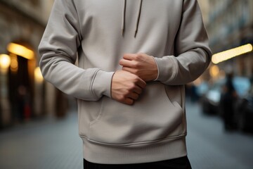 Fototapeta premium Front view of an unidentifiable person standing on a city street wearing a plain hoodie, mockup
